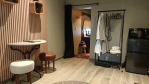 Un baño moderno con un tocador de madera, un lavabo y un inodoro. Hay una zona de ducha con puerta de vidrio y un perchero.