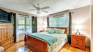 Ein Schlafzimmer mit einem hölzernen Bett, einem Nachttisch, einer Kommode, einem Deckenventilator und Fenstern mit Vorhängen.