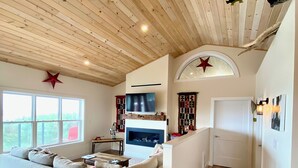 A spacious living area with a wooden ceiling, a large sofa, a fireplace, and a TV.