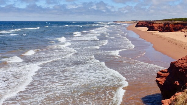 A beach with waves, a sandy shore, and a cliff.