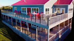 A two-story house with a red roof, a covered deck with red chairs, and a blue exterior.