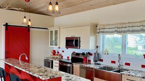 A modern kitchen with a red island, stainless steel appliances, and pendant lighting.