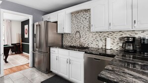 A modern kitchen with white cabinets, a stainless steel refrigerator, a dishwasher, and a black marble countertop. - HOT TUB Tranquil Escape Pool Gym (Round Rock)