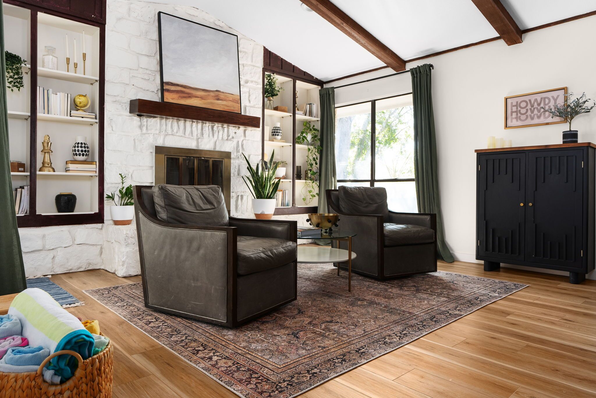 A living room with two leather armchairs, a fireplace, a bookshelf, and a large window with curtains.