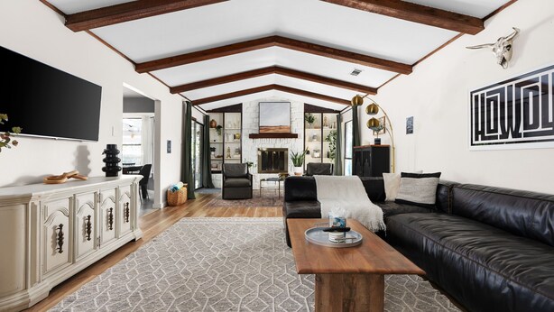 A spacious living room with a high ceiling, exposed wooden beams, a fireplace, a black leather sofa, and a patterned rug. - HOT TUB Tranquil Escape Pool Gym (Round Rock)