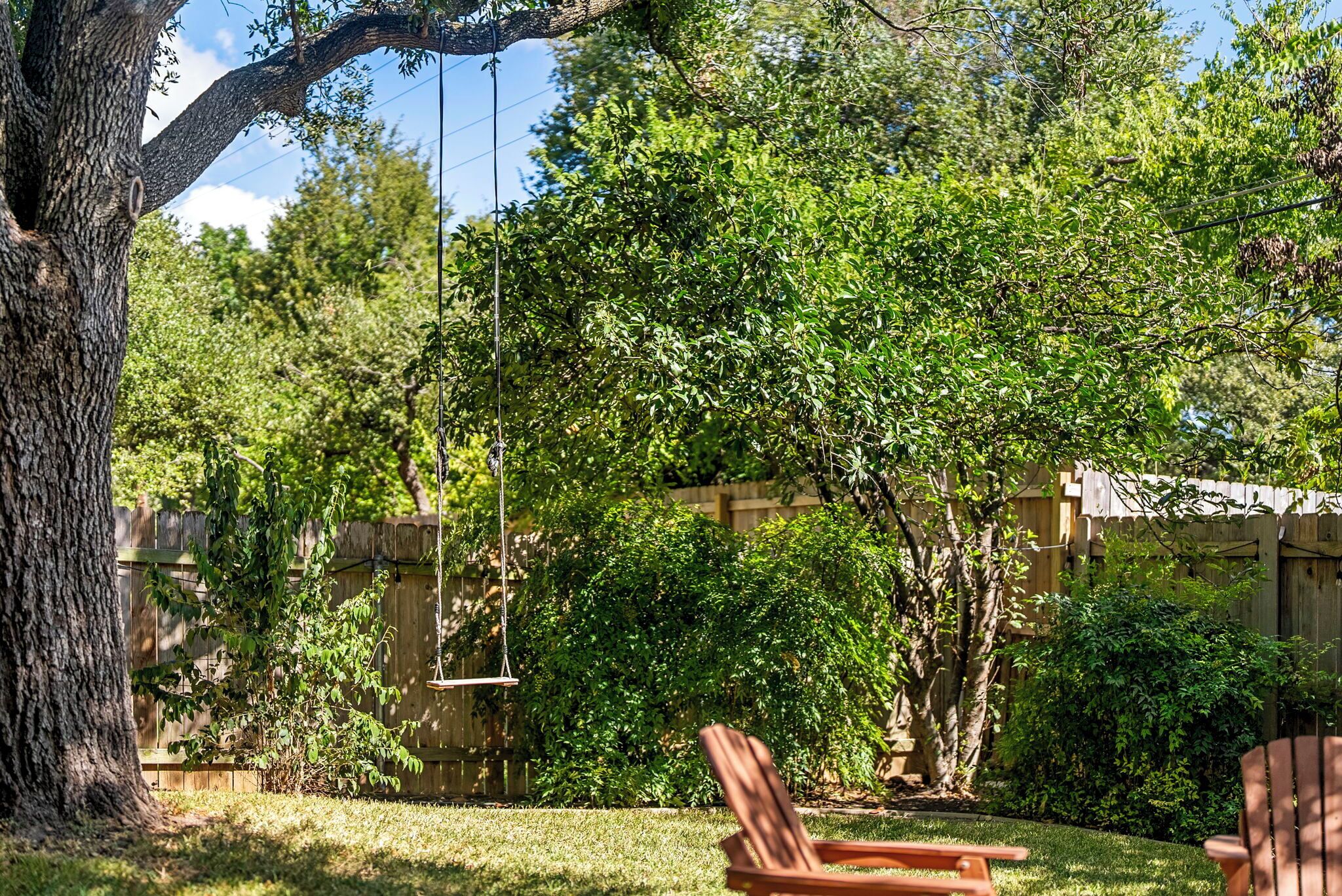 A backyard with a swing set, two wooden chairs, and a wooden fence.