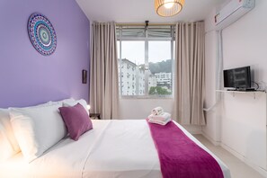 A hotel room with a bed, a TV, a window with curtains, and a city view.