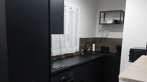 Una cocina moderna con armarios negros, horno integrado, un lavabo y una cafetera.