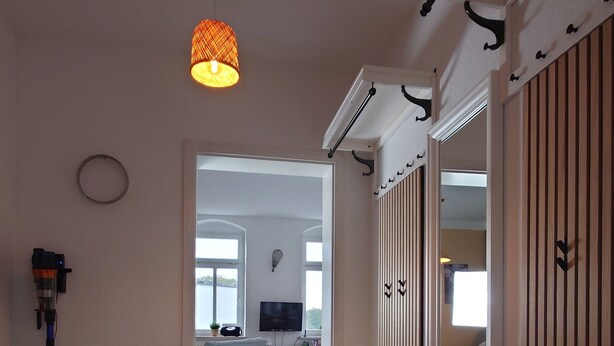 Ein Hotelzimmer mit Schachbrettboden, einer weißen Bank, einer Hängelampe und Blick auf die Küche und den Wohnbereich durch eine offene Tür.