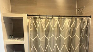A bathroom with a shower curtain featuring a geometric pattern, a toilet, and a shelf with folded towels.