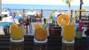 Drie glazen sinaasappelsap met rietjes op een tafel in een restaurant aan zee.