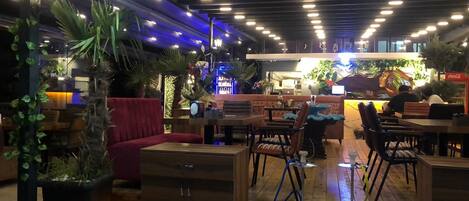 Un restaurante con mobiliario de madera, plantas en macetas y una zona de bar.