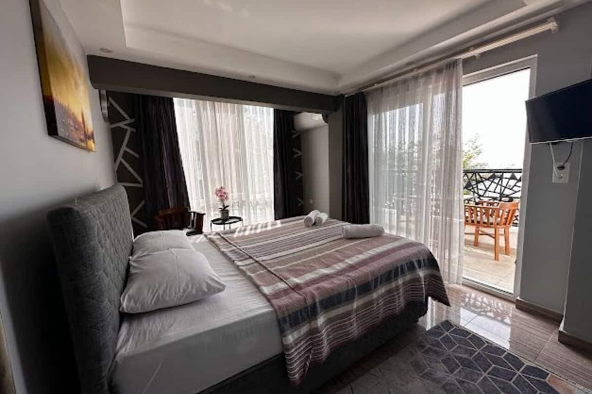 Moderni hotellihuone, jossa on suuri sänky, taulutelevisio ja parveke, jossa on ulkokalusteita.