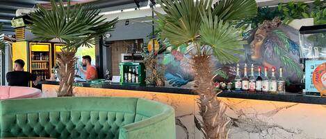 Un interior de restaurante con cabinas tapizadas de verde, una encimera de mármol y un mural en la pared.