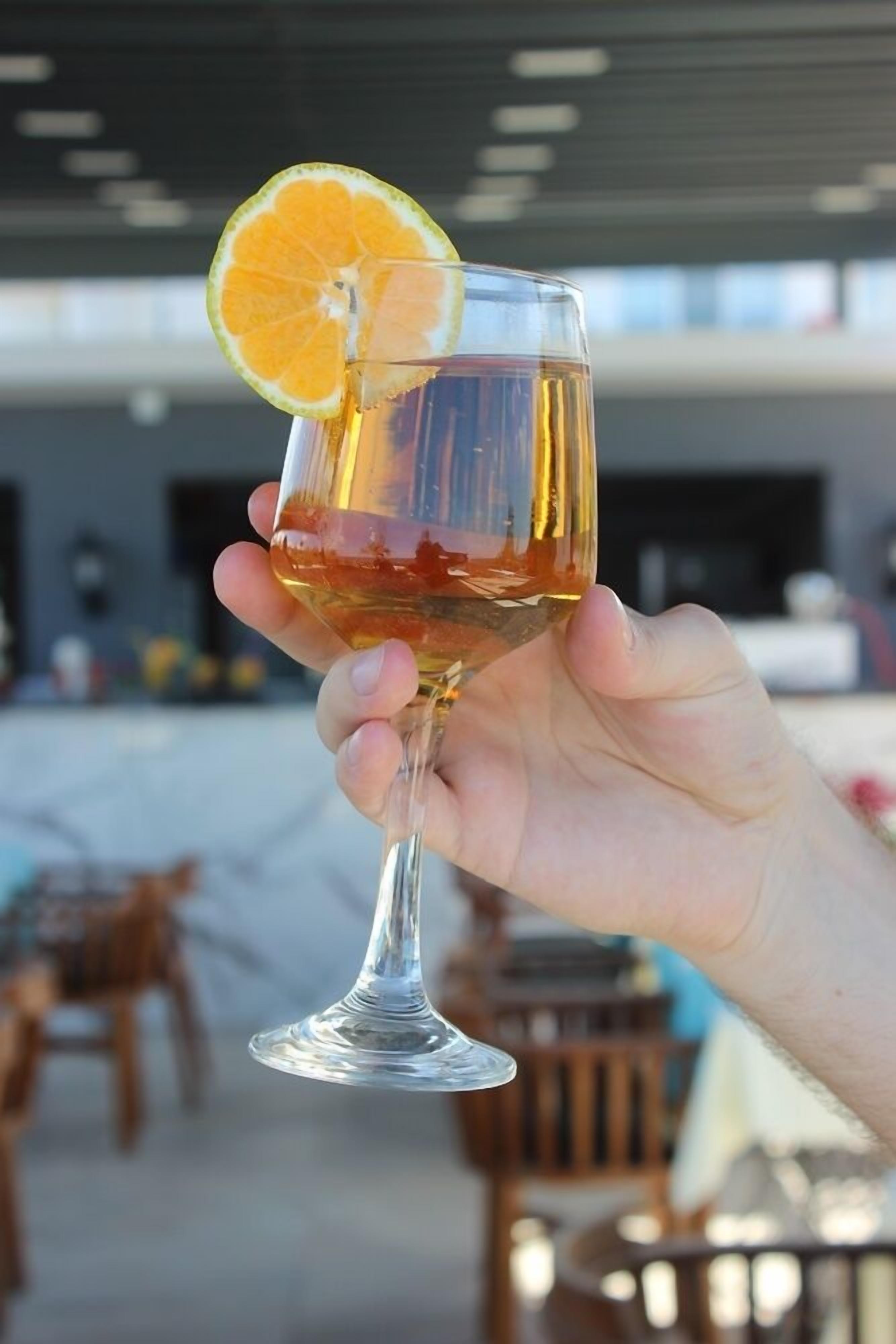 A hand holding a glass with a slice of orange on the rim.