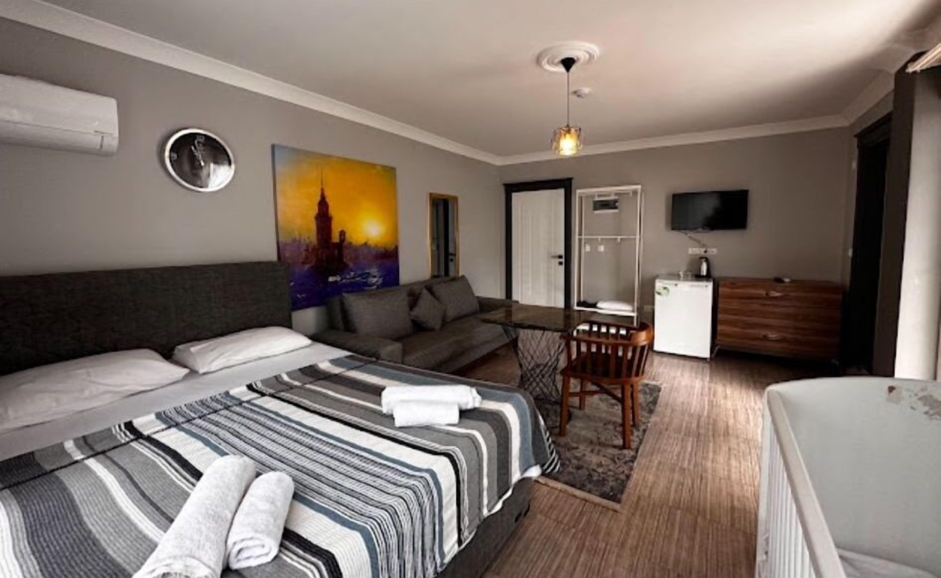 A hotel room with a large bed, a sofa, a desk, a chair, a television, and a painting on the wall.
