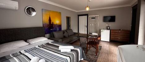 A hotel room with a large bed, a sofa, a desk, a chair, a television, and a painting on the wall.