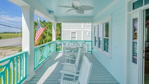Eine Veranda mit Tisch, Stühlen und Deckenventilator, mit Blick auf ein Haus.