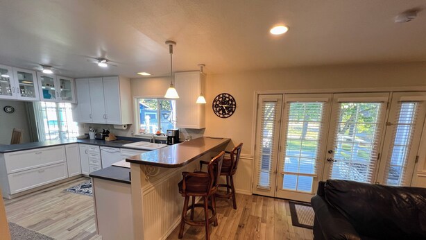 A modern kitchen with white cabinets, a central island with stools, pendant lighting, and a view through the glass doors to the outside. - Your Peaceful Home on the Klamath River (Montague)