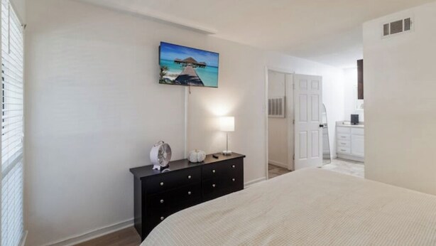 A bedroom with a bed, a dresser, a lamp, and a painting of a beach scene. - 50 Yard Line

 (College Station)
