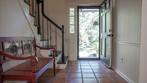 A hallway with a wooden bench, a staircase with black railings, and a door leading outside.