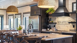 Una cocina moderna con una isla central, muebles oscuros, electrodomésticos de acero inoxidable y un letrero que dice "BON APPETIT".
