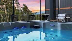 Un jacuzzi con vistas a un atardecer, una parrilla para barbacoa y un patio con sillas.