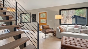 A modern living room with a staircase, a sofa, a chair, and a dining area.