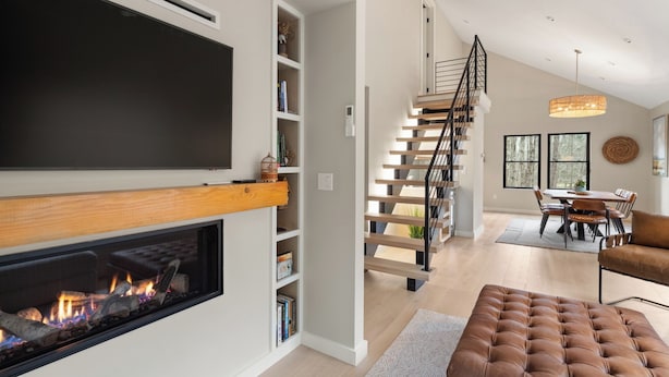 A modern living room with a fireplace, a staircase, and a dining area.