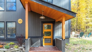 A modern building with a yellow door, numbered 981, and a covered porch with a hanging light fixture.