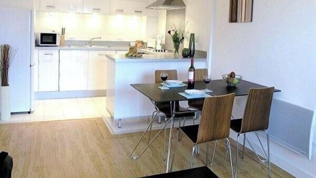 Une cuisine moderne avec des meubles blancs, un îlot central et un coin repas comprenant une table et des chaises.