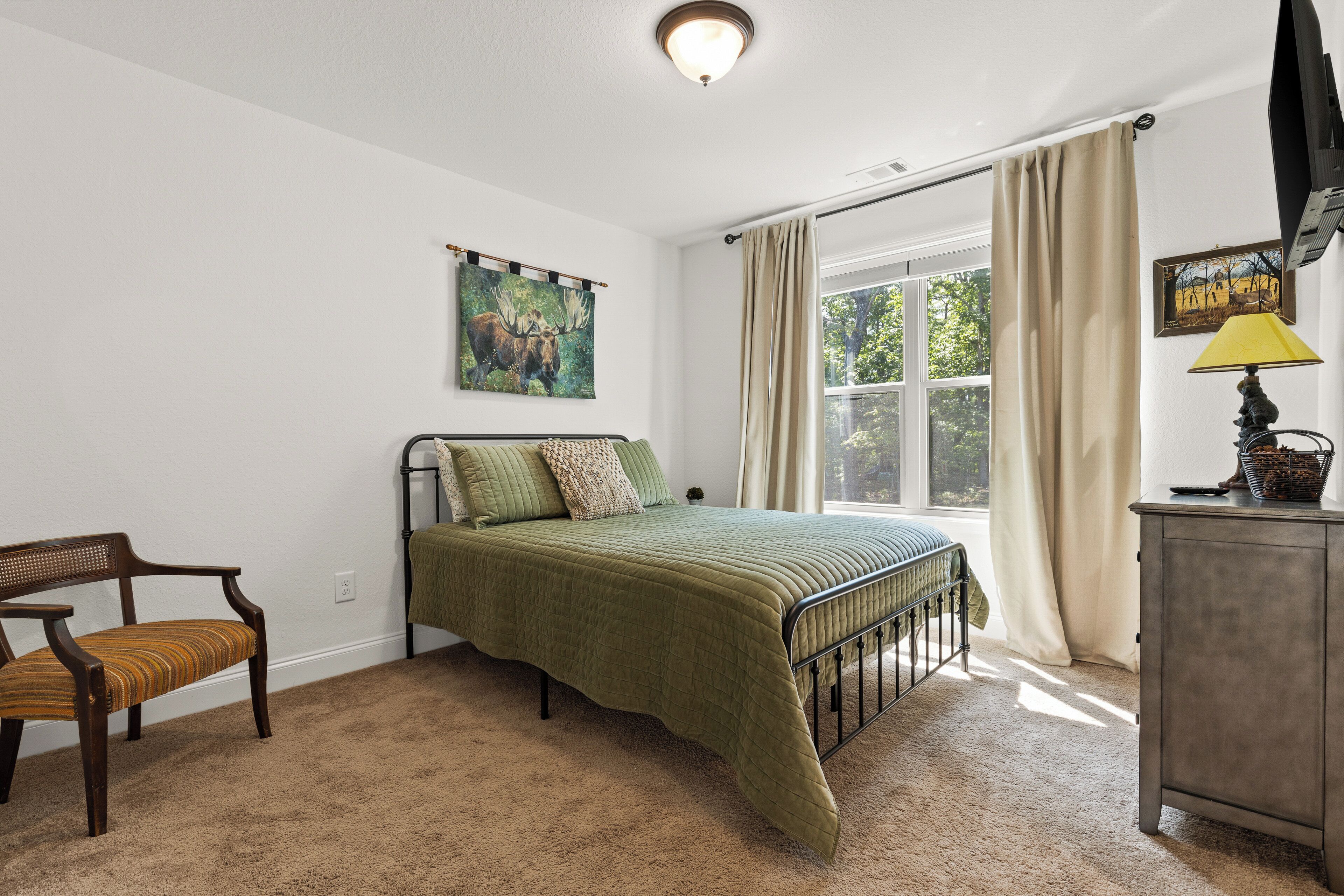 A bedroom with a bed, a chair, a dresser, and a window with curtains.