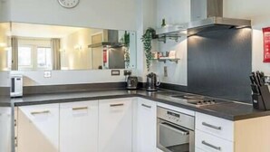 A modern kitchen with white cabinets, a stainless steel range hood, and a built-in oven.