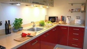 A kitchen with red cabinets, a sink, a microwave, a toaster, and various kitchen items on the counter.