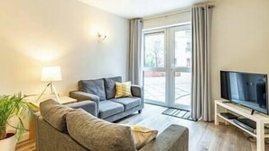 A modern living room with a grey sofa, a TV on a wooden stand, and a large window with curtains.