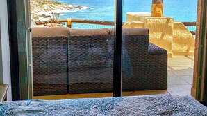 Un balcon avec des meubles en osier, une vue sur l’océan et un mur en pierre.
