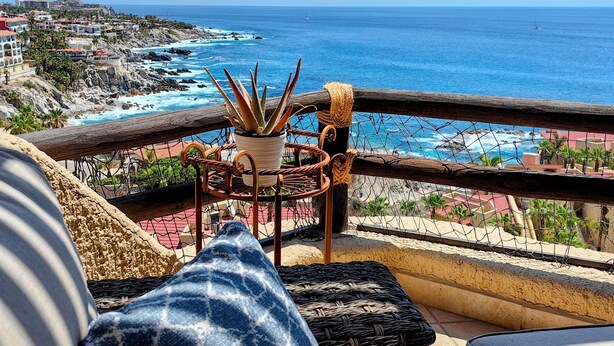 Un balcon avec vue sur l’océan, une plante en pot et une chaise en osier.