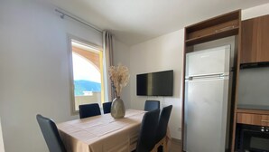 Un'area pranzo con un tavolo apparecchiato per quattro persone, una TV a schermo piatto montata a parete e un frigorifero nella zona cucina.