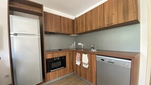 Una cucina compatta con mobili in legno, forno integrato, lavastoviglie e frigorifero in acciaio inossidabile.