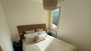 Un letto rifatto con cura, una testiera in legno, una lampada da comodino e una finestra con vista su un paesaggio montuoso.