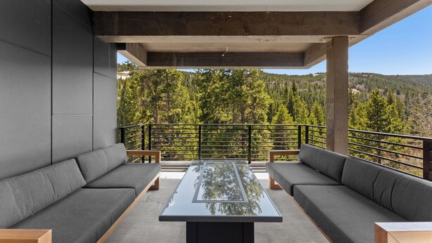A modern outdoor seating area with a glass-top table, grey sofas, and a view of a forested hillside. - Iwtbk4 (Keystone)