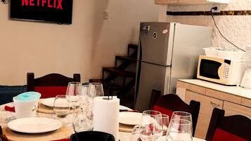 A dining area with a table set for four, a TV displaying 'NETFLIX,' a refrigerator, and a microwave in the background.