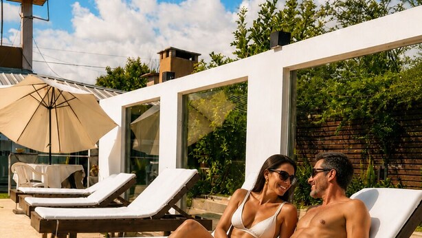 A couple relaxing on sun loungers by a poolside with a modern white building and a water tank in the background. - Buenos Aires de Ezeiza Resort Vacacional - Dos Departamentos (La Unión)