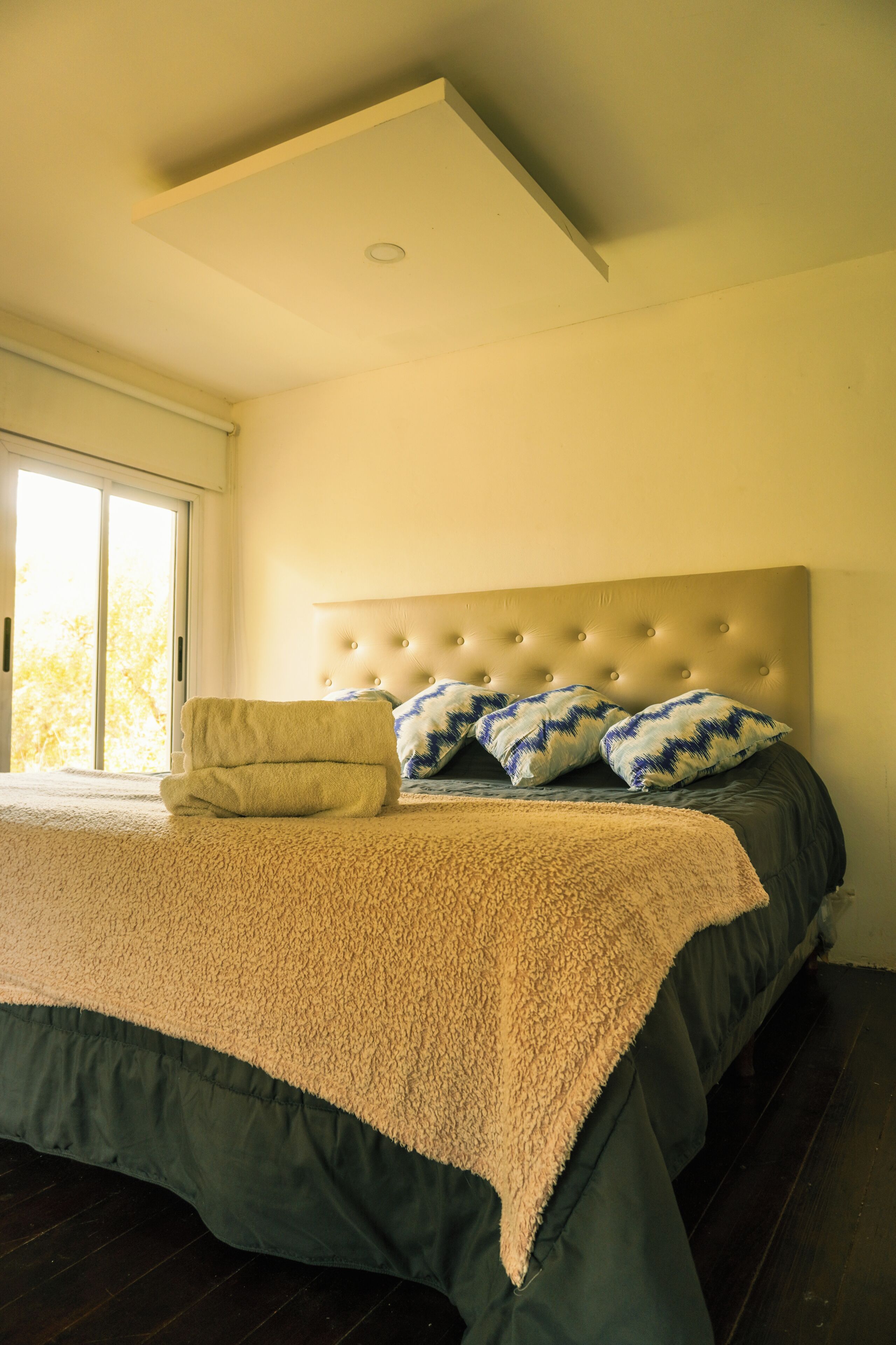 A bedroom with a large bed, a headboard, and a view through a sliding door.