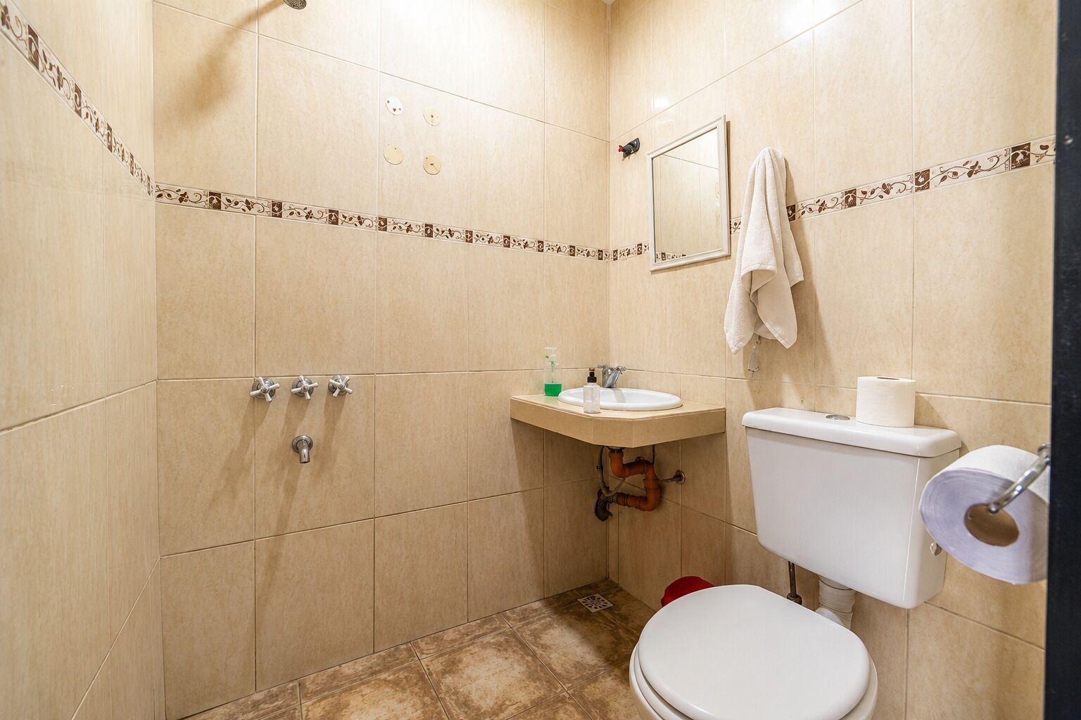Een badkamer met beige tegels, een wit toilet, een wastafel met spiegel en een handdoek aan de muur.