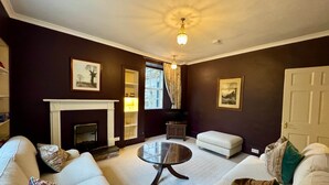A living room with a fireplace, white sofas, a round coffee table, and a television. - Charming 1700s Country Cottage on a Private Estate (Stirling)