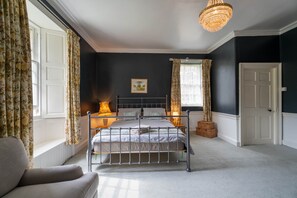A bedroom with a metal bed frame, two bedside lamps, a chandelier, and a window with curtains.
