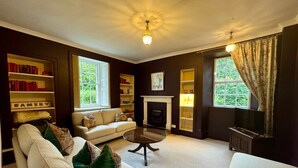 A living room with a fireplace, bookshelves, a sofa, and a television. - Charming 1700s Country Cottage on a Private Estate (Stirling)