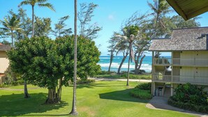 A beachfront property with a well-maintained lawn, a two-story building with a balcony, and a view of the ocean. - Ocean View, Split AC, King Bed, Wifi, Pool Hot Tub (Kapaa)