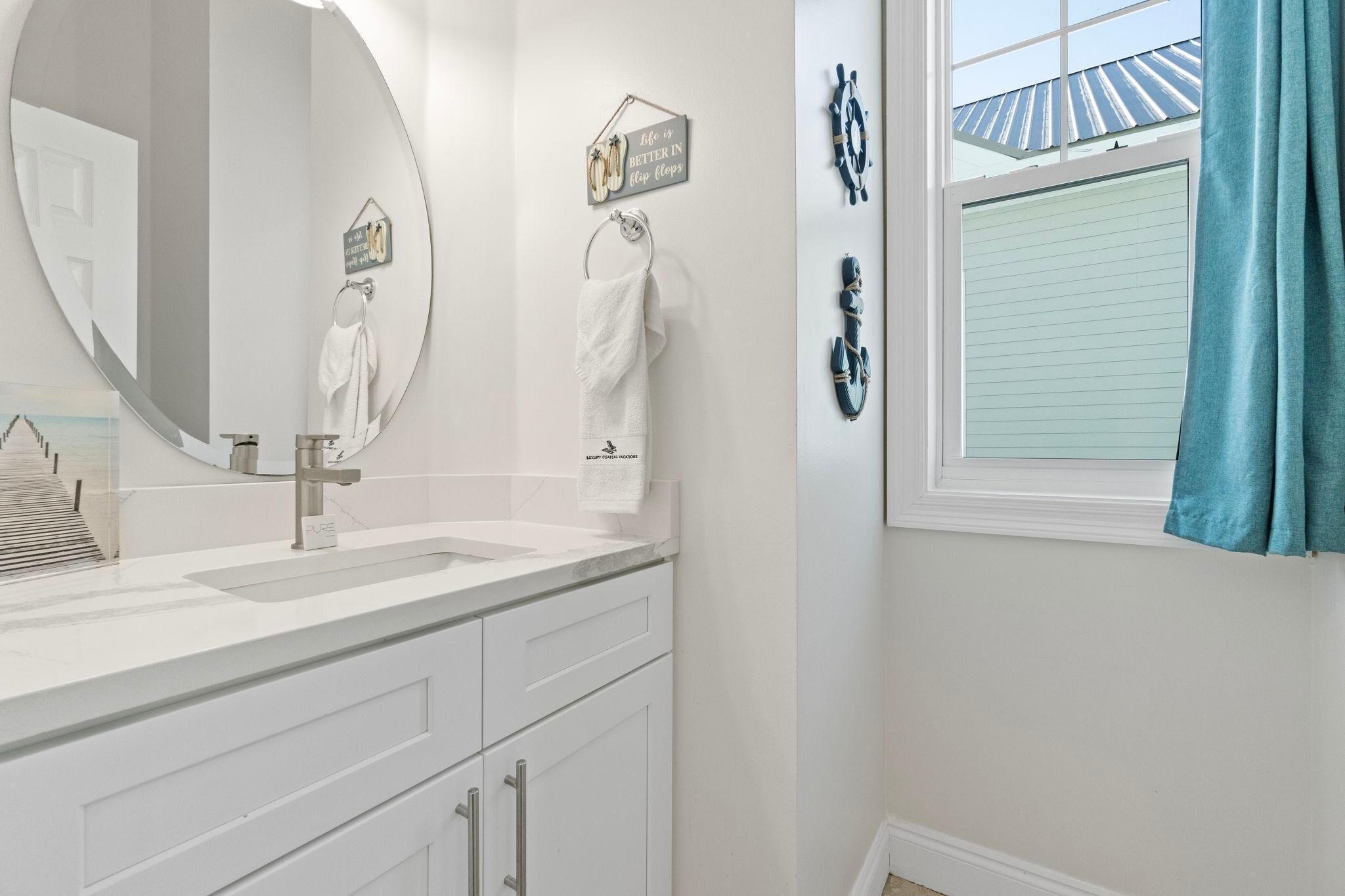 A bathroom with a large mirror, white cabinets, a sink, and a window with a view of the roof.